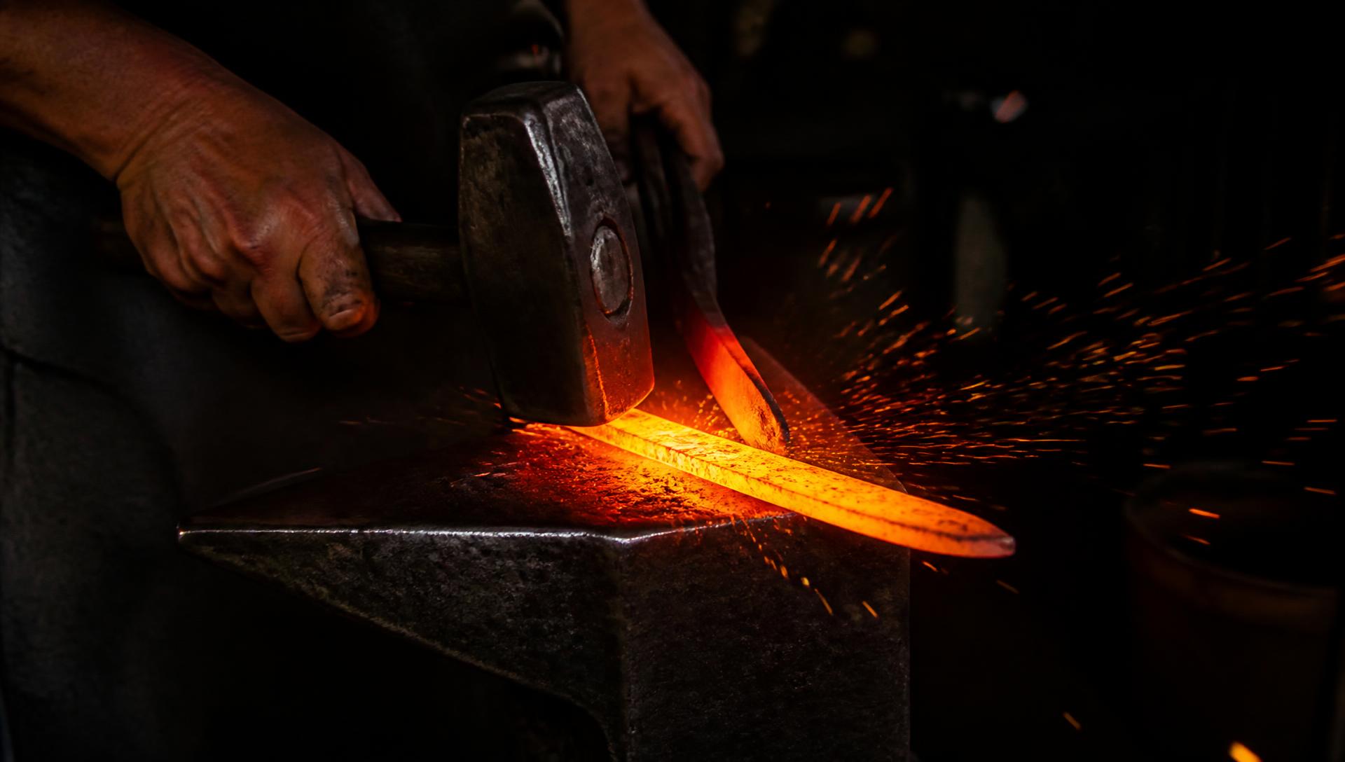Blacksmith hammering a glowing hot blade on an anvil as sparks fly
